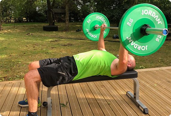 Client bench pressing a barbell on the decking outside the studio